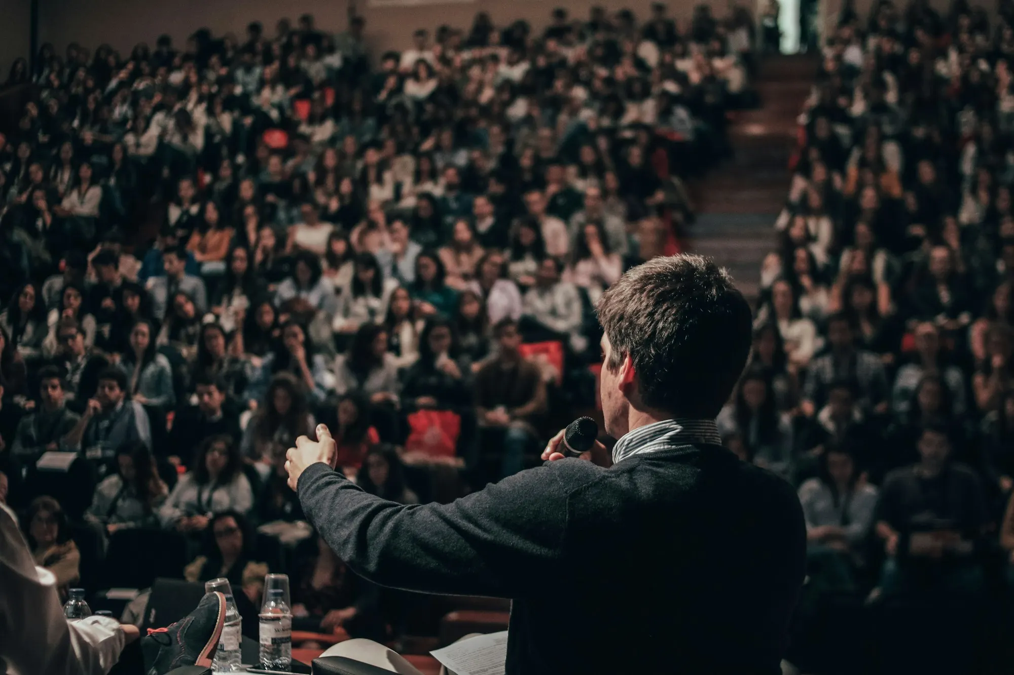 Palestrante de costas diante de uma plateia numerosa.